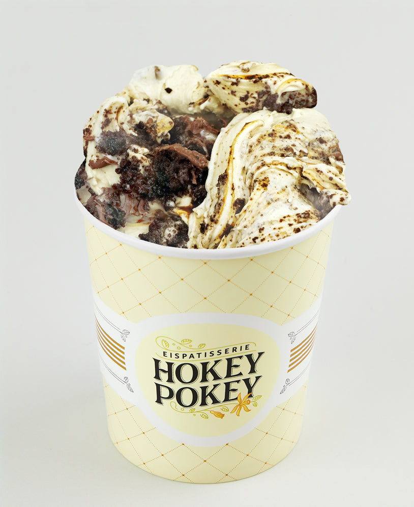Becher mit Bananen-Dulce-de-Leche-Eis der Eispatisserie Hokey Pokey Berlin, durchzogen mit Karamell und Brownie-Stücken, serviert im gelben Markenbecher vor hellem Hintergrund.