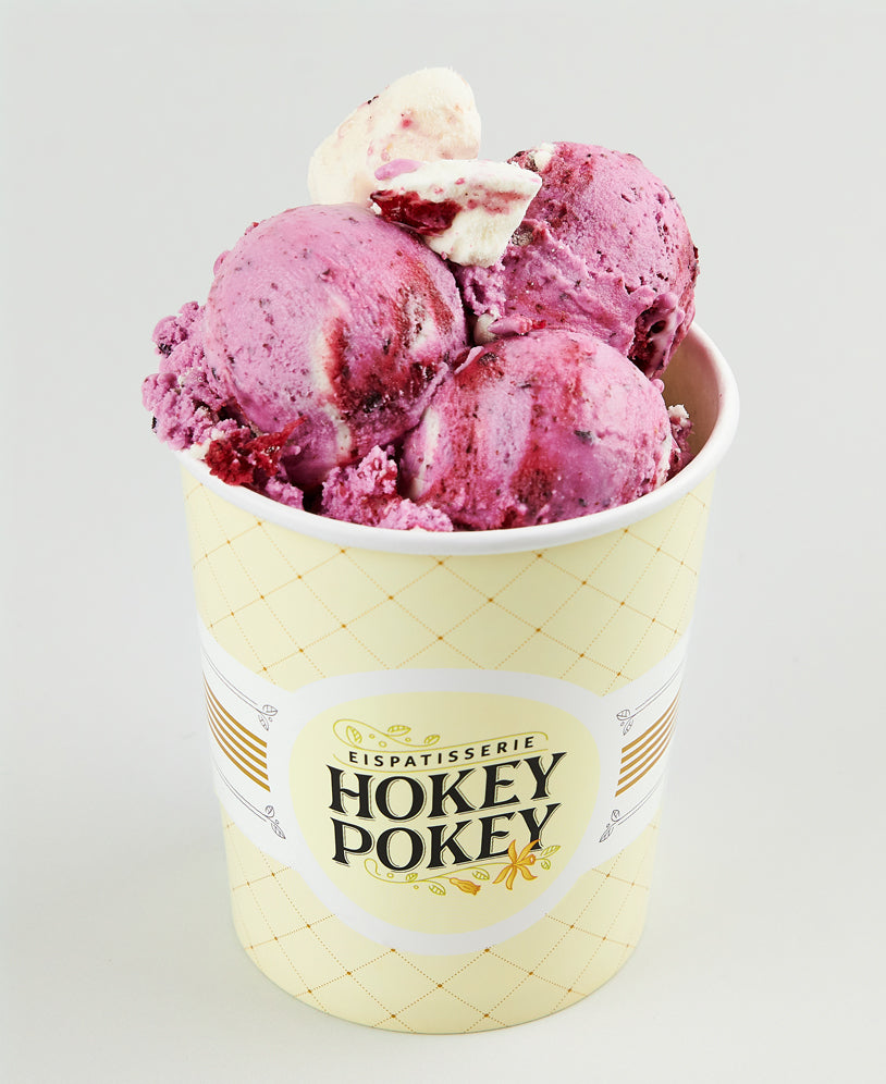 Becher mit fruchtigem Blaubeereis und Baiser-Stücken der Eispatisserie Hokey Pokey Berlin, serviert in einem gebrandeten Designbecher auf hellem Hintergrund.