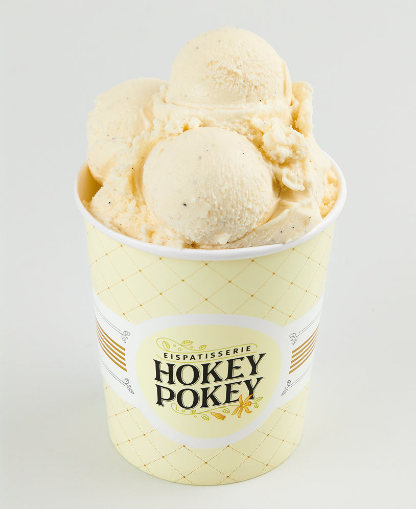 Becher mit klassischem Bourbon-Vanilleeis der Eispatisserie Hokey Pokey Berlin, sichtbar mit echter Vanille verfeinert, serviert im gelben Markenbecher vor hellem Hintergrund.
