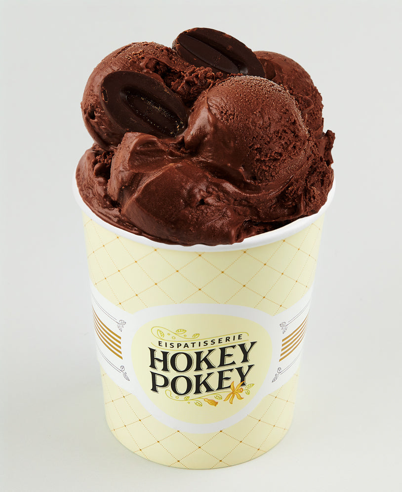 Becher mit dunklem Kaffee-Schokoladeneis der Eispatisserie Hokey Pokey Berlin, verziert mit Schokobohnen, serviert im gelben Logo-Becher vor hellem Hintergrund – intensiv und cremig.