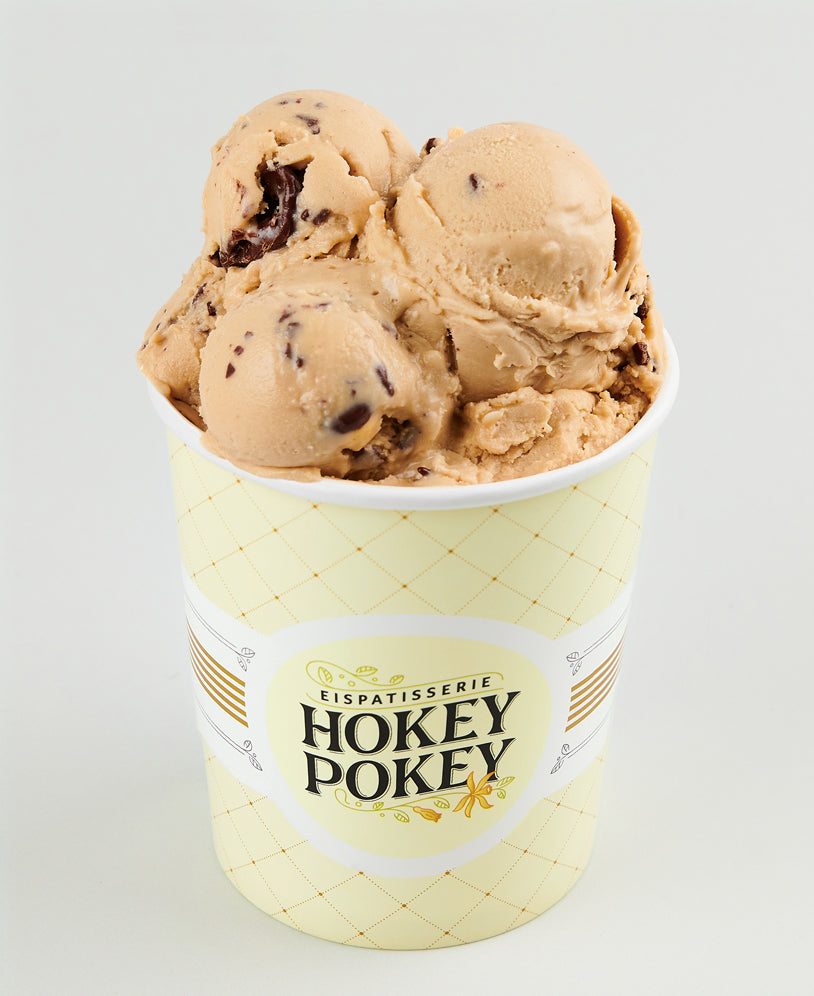 Becher mit Haselnusseis und Schokostückchen der Eispatisserie Hokey Pokey Berlin, serviert im gelben Markenbecher vor neutralem Hintergrund – cremig und handgemacht.
