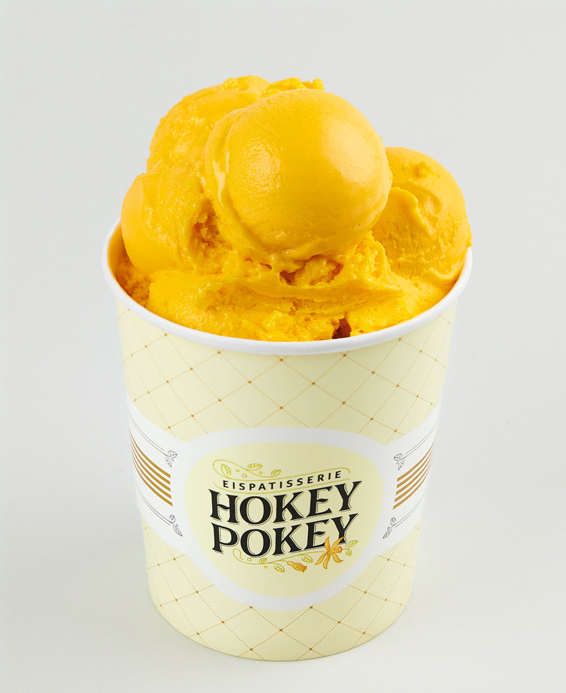 Becher mit leuchtend gelbem Mangosorbet der Eispatisserie Hokey Pokey Berlin, serviert im markanten Logo-Becher auf hellem Hintergrund – fruchtig, vegan und erfrischend.