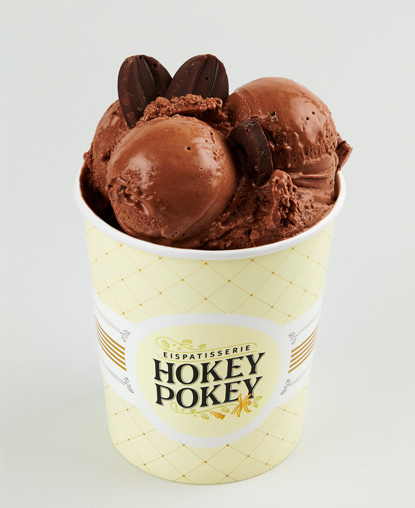 Becher mit veganem Schokosorbet der Eispatisserie Hokey Pokey Berlin, intensiv dunkel und garniert mit Schokodrops, serviert im gelben Logo-Becher vor hellem Hintergrund.