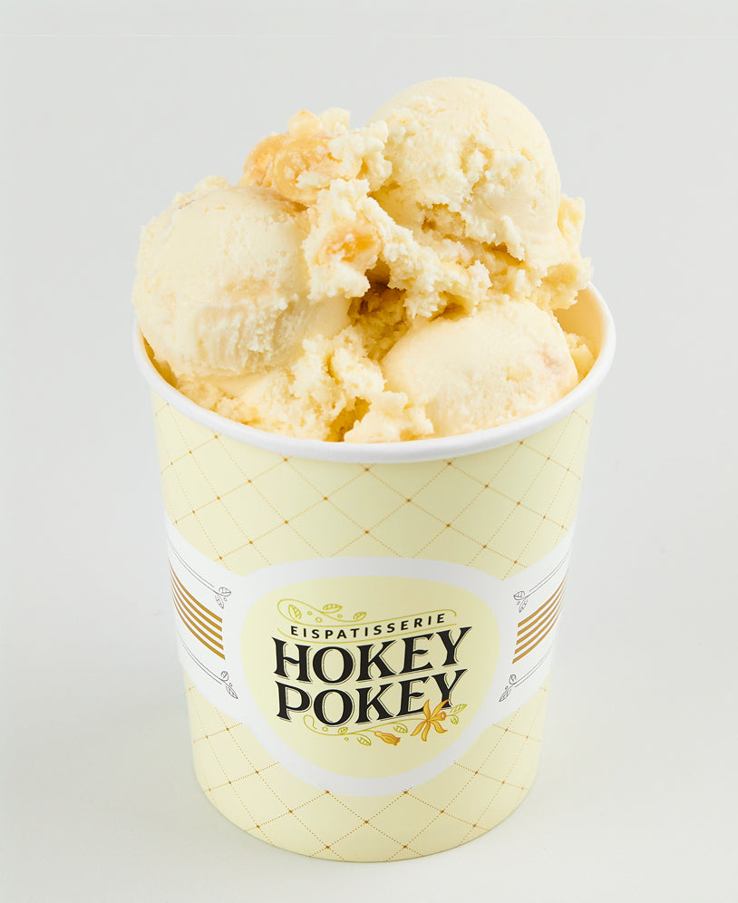 Becher mit weißer Schokoladen-Macadamia-Eiscreme der Eispatisserie Hokey Pokey Berlin, serviert im gebrandeten Becher vor hellem Hintergrund – nussig, süß und cremig.